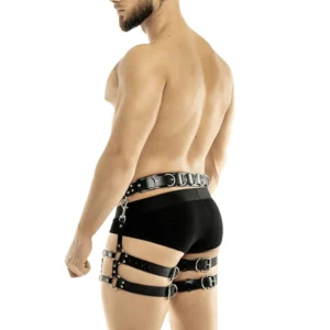 Black adjustable body harness rear view with multiple strap detail, worn by bearded male model with black briefs, studio lighting