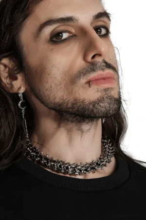 Gothic spine choker three-quarter side angle worn by long-haired male model paired with feather earrings, studio backdrop