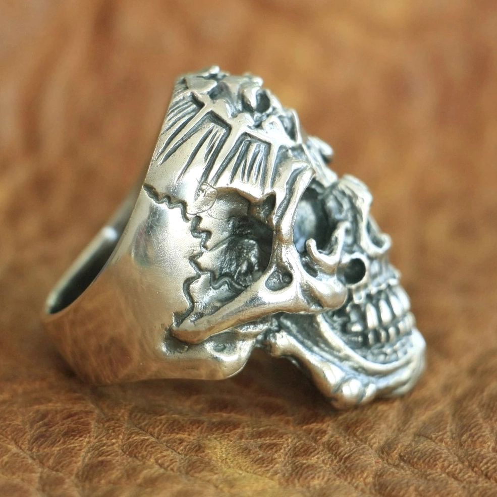 Wide silver skull ring side flat lay on leather showing full band width and carved features