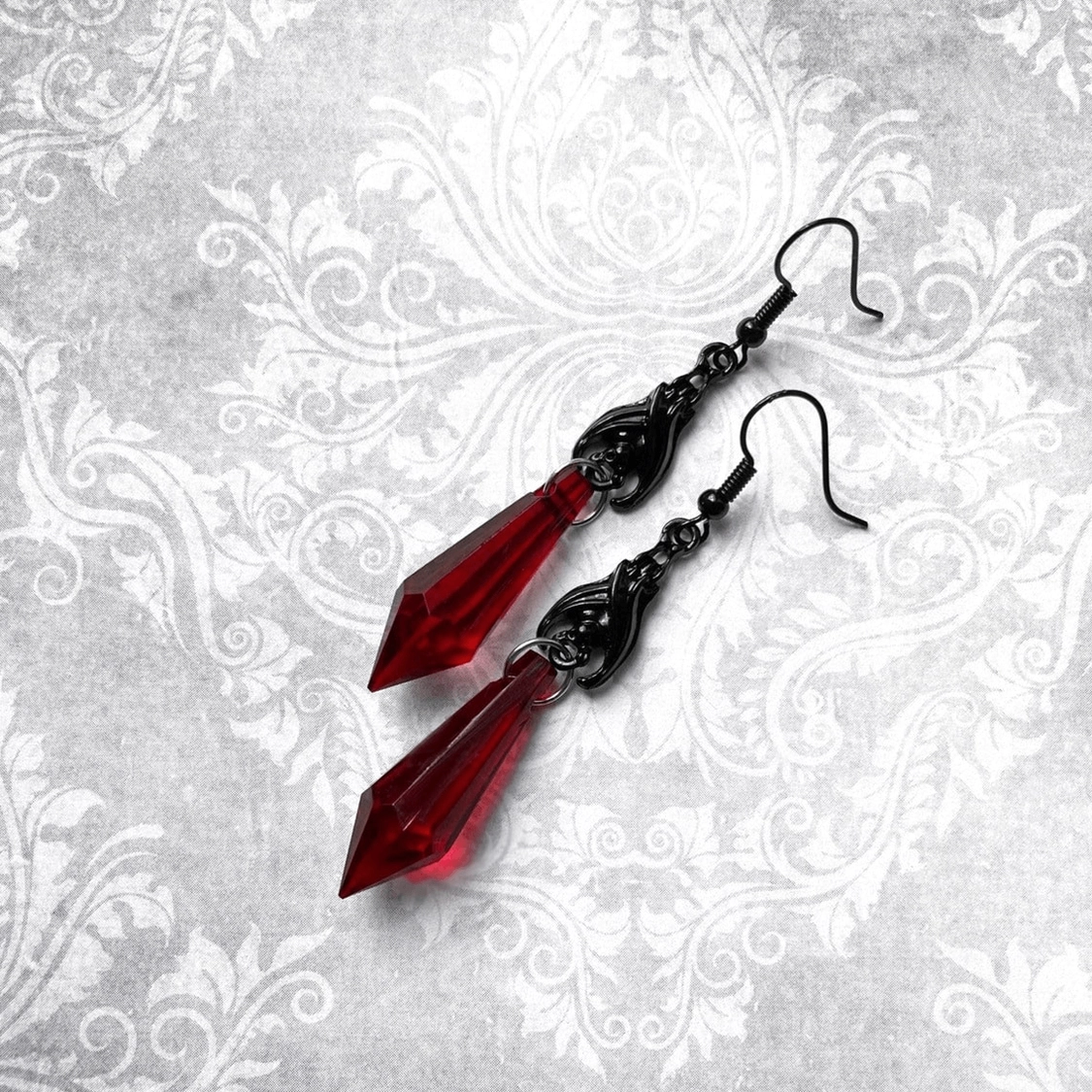 Black filigree bat earrings with red faceted teardrop charms on vintage damask background