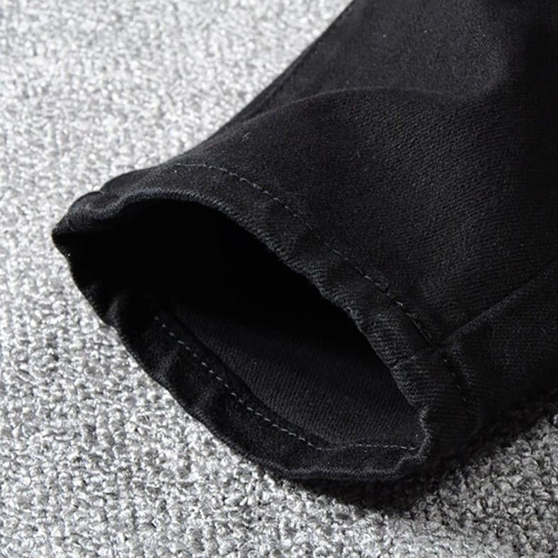 Hem cuff and ankle opening detail of slim fit black biker jeans showing standard denim stitching and fitted cut