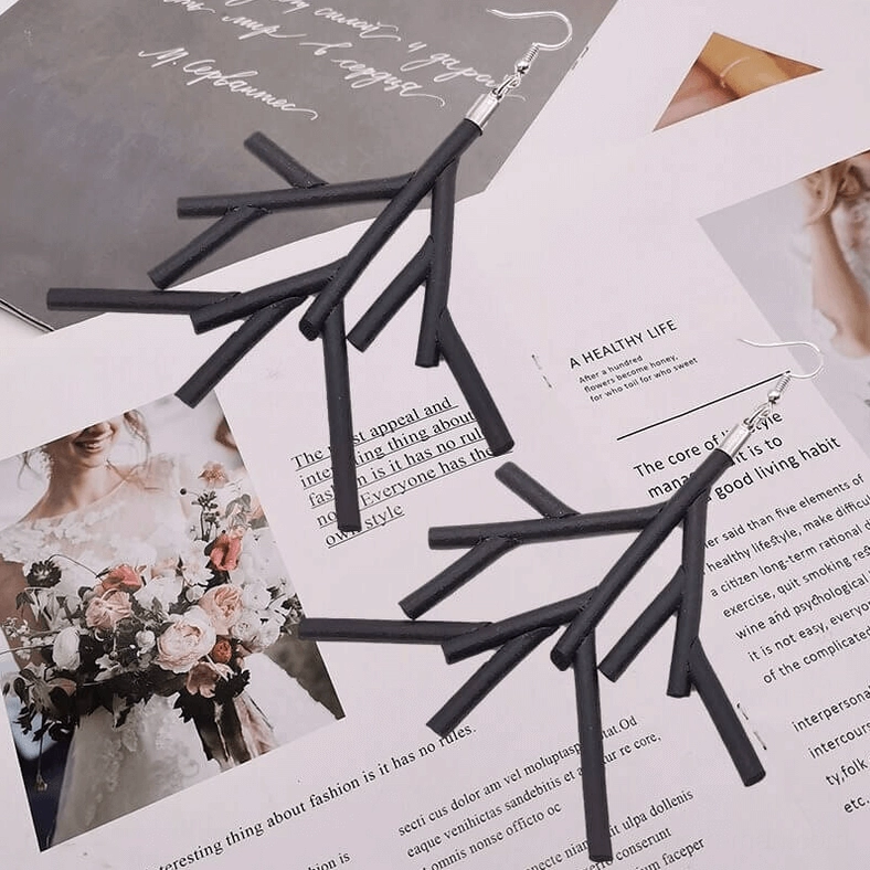 Two pairs of black branch dangle earrings flat lay on fashion magazine pages with printed decor, gothic alternative fashion jewelry