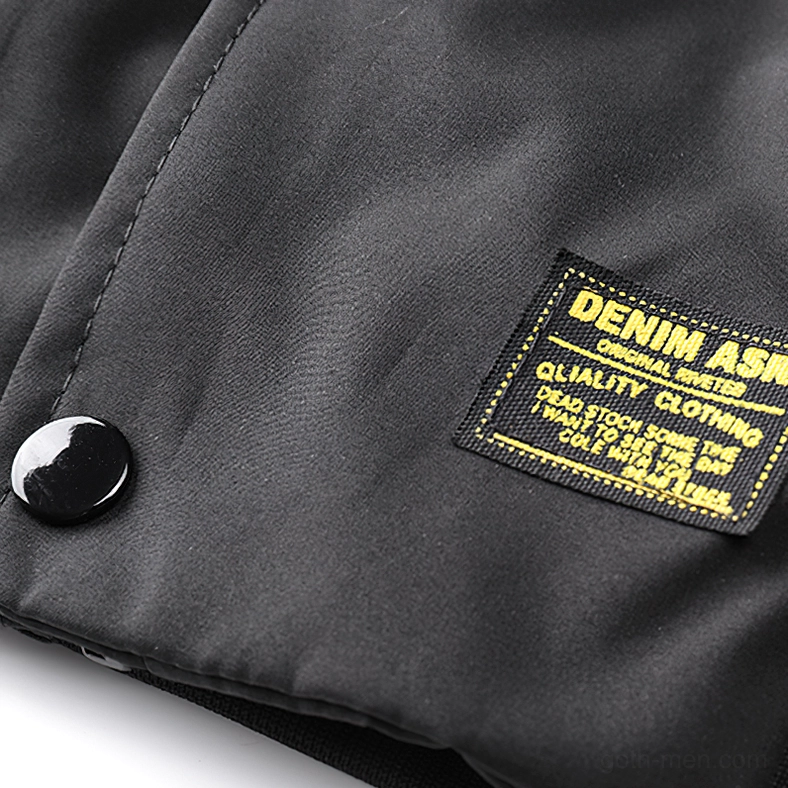 Black cargo bomber jacket hem detail showing yellow embroidered brand patch and snap buttons