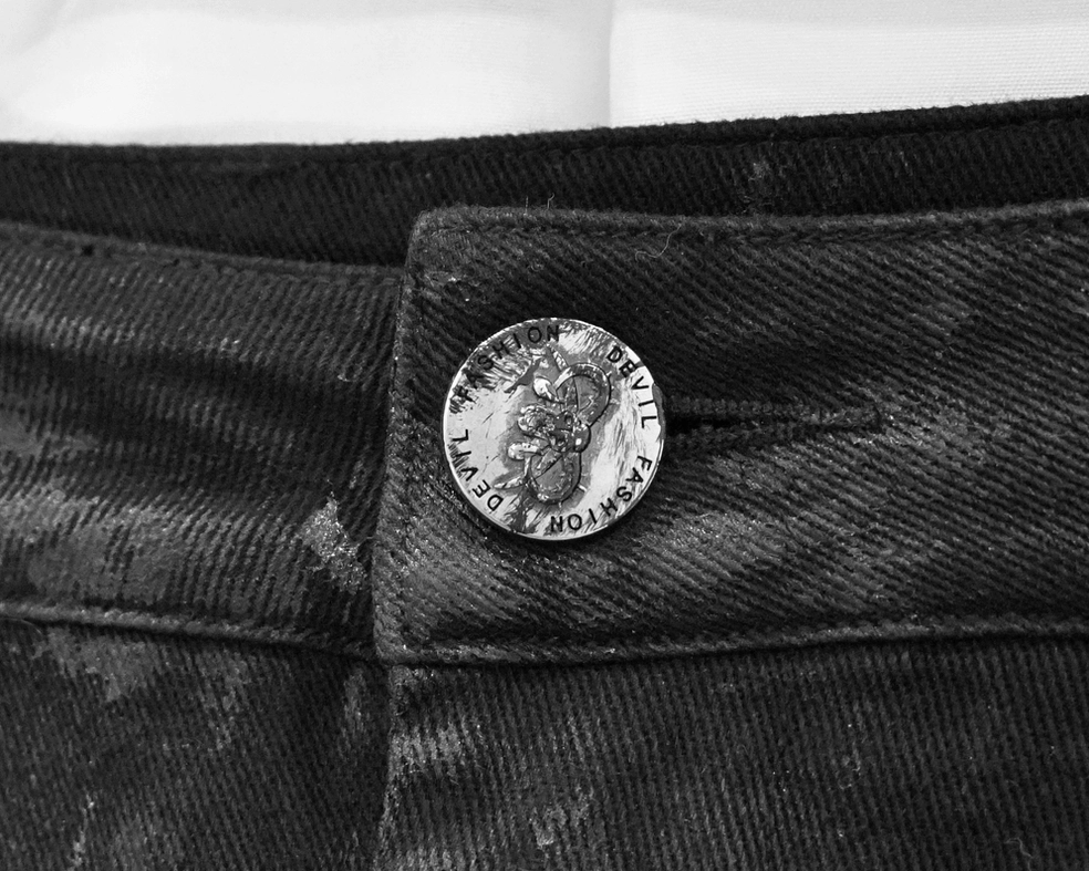 Close-up detail of black trouser waistband with branded metal button and faded denim texture
