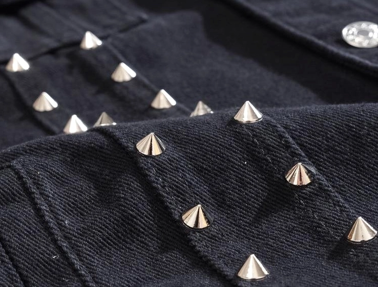 Flat close-up of silver cone spike stud detail on black twill denim fabric