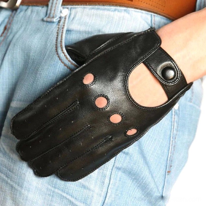 Oblique front view of black genuine leather gothic gloves beside denim jeans pocket, showcasing circular ventilation holes and wrist button