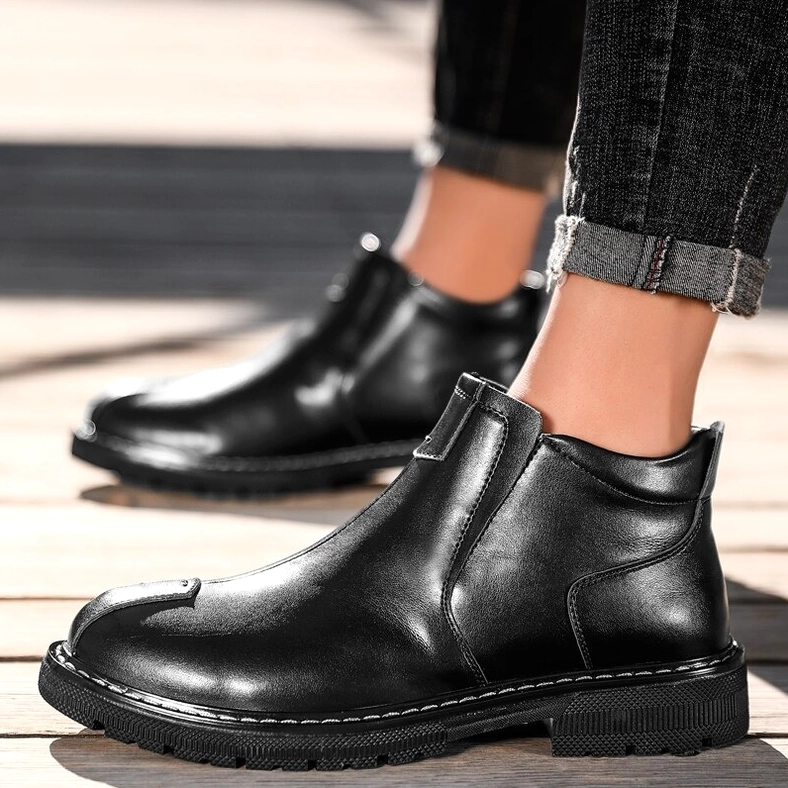 Gothic ankle boot for men in black leather, worn with rolled dark jeans on wooden outdoor background
