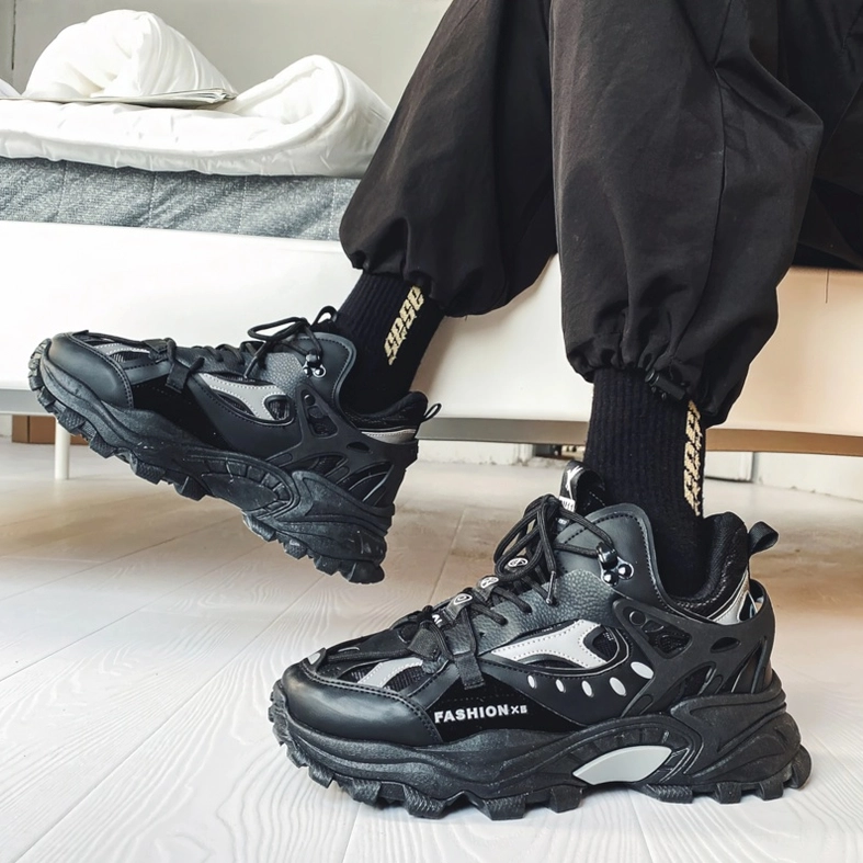 Black gothic alternative chunky sneakers on model with dark track pants and branded socks, bedroom floor styling