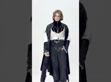 Blonde male model wearing black gothic long cloak with cross necklace, layered with high-waisted trousers and white inner shirt