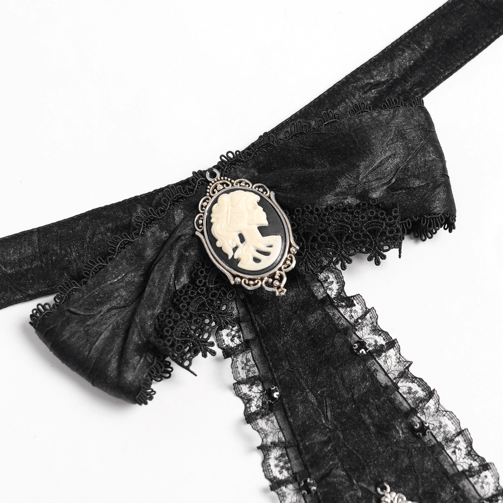Close-up detail of black gothic jabot choker featuring cameo portrait brooch, ruffled lace edging, and textured black fabric