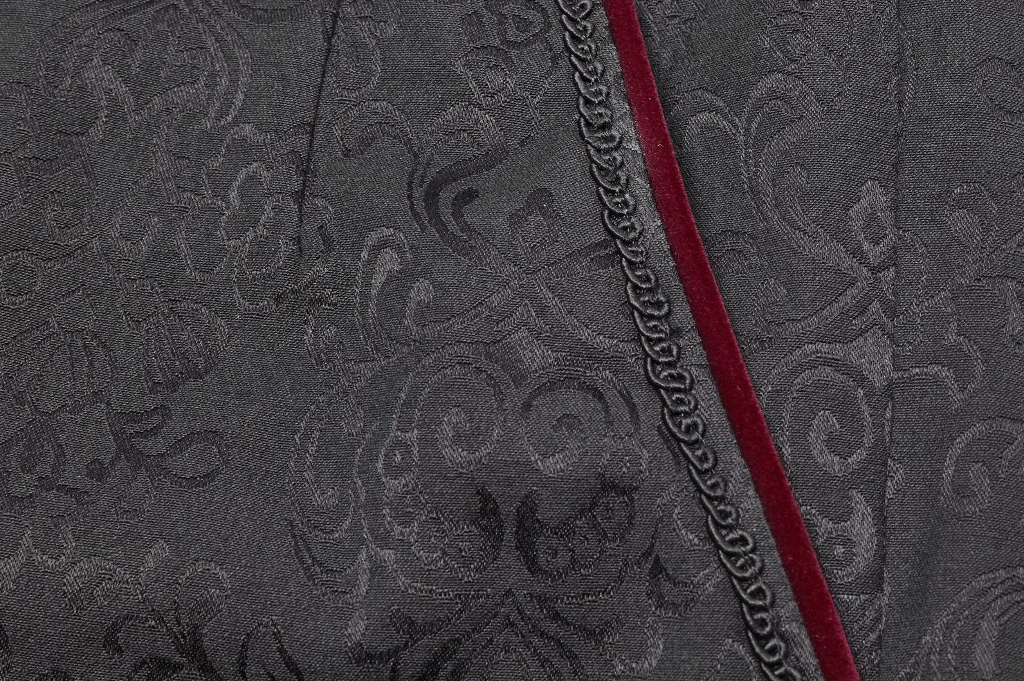Black gothic jacquard slim-fit pants fabric close-up displaying embroidered chain trim, red velvet stripe, and ornate jacquard weave