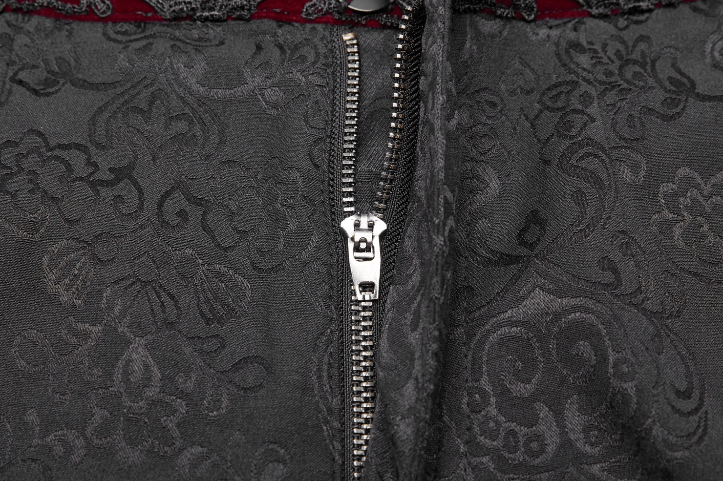 Black gothic jacquard slim-fit pants front waist close-up showing metal zipper fly and floral jacquard fabric with red accent trim