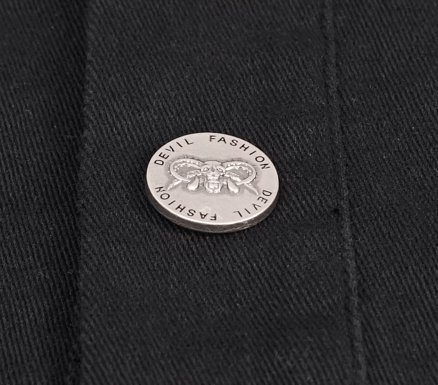Close-up of branded metal button on black gothic punk vest featuring devil fashion logo and twill fabric texture detail