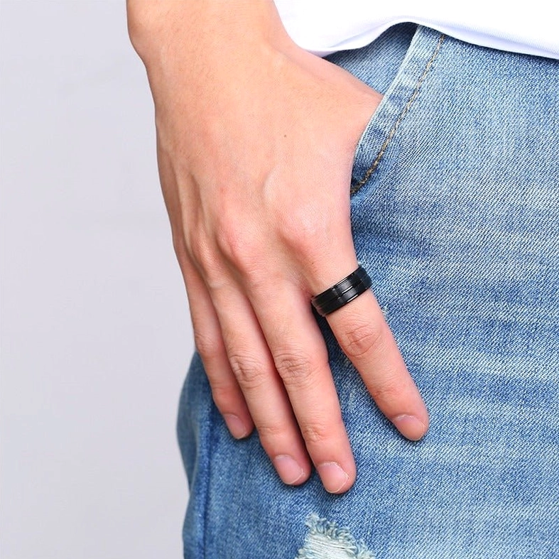 Men's black metal gothic ring worn on index finger close-up with denim background, alternative jewelry styling