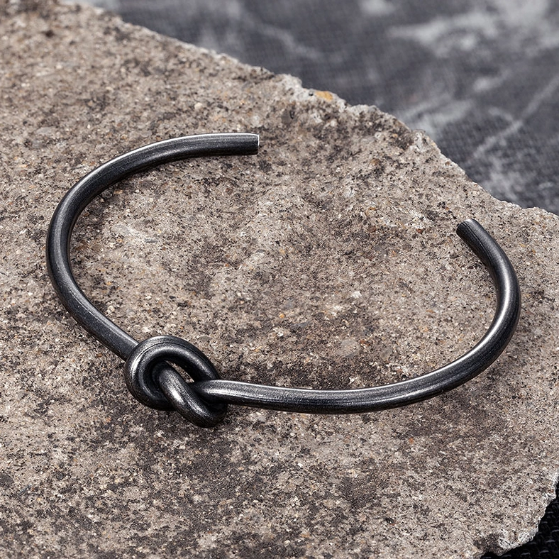 Matte black knotted stainless steel bracelet close-up detail on stone surface showing knot craftsmanship