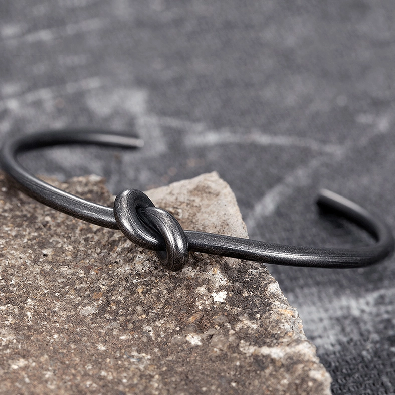 Black knotted open cuff bracelet flat lay from above on natural stone background with knot detail visible