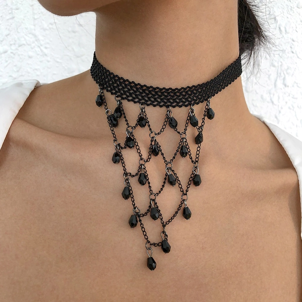 Woman wearing black lace gothic choker necklace with teardrop pendants, styled on neck and upper chest, side front view with white textured wall background
