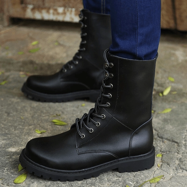 Black combat boots styled with blue jeans front-side view, showcasing round toe and matte black leather upper on outdoor ground with leaves