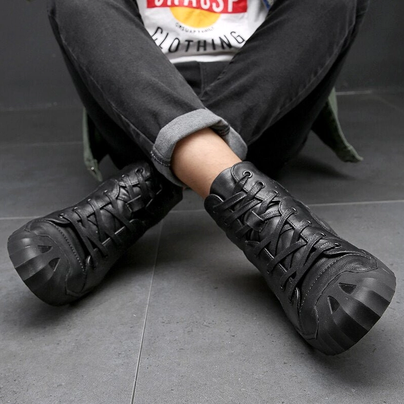 Black leather high-top gothic sneakers worn by male model seated with rolled denim in indoor setting