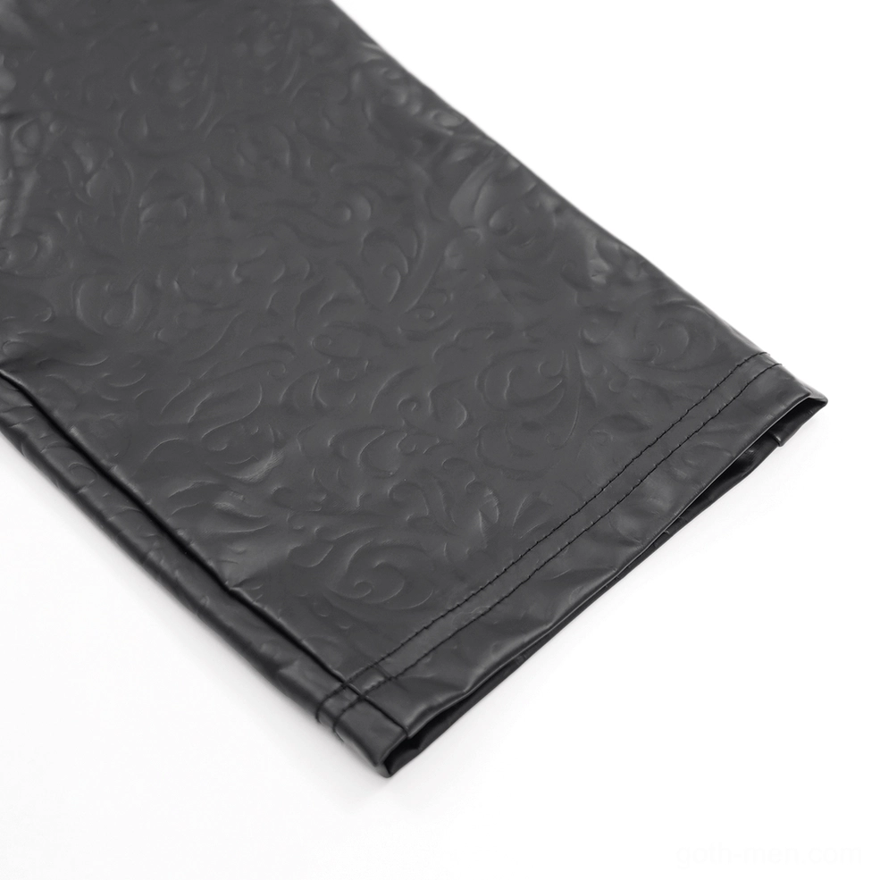 Flat lay close-up of black leather pants leg panel showing finished hem and vintage embossed pattern
