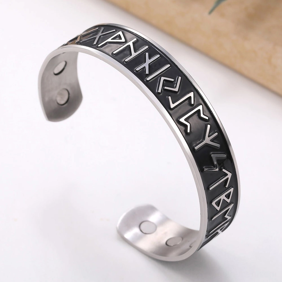 Black and silver gothic Nordic rune open cuff bracelet showing internal magnetic dots, angled view on floral background
