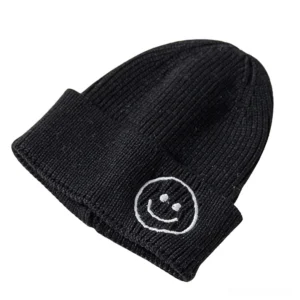 Black ribbed knit beanie with white outlined smiley face embroidery, studio shot on white background