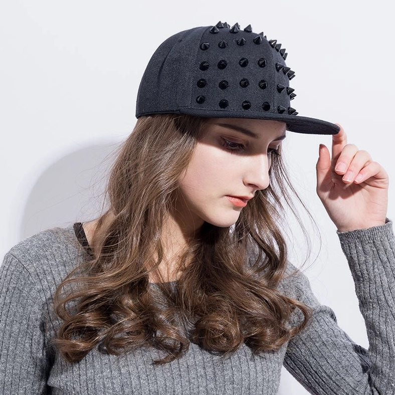 Model adjusting all-black spike gothic snapback baseball cap, right side three-quarter view with long hair