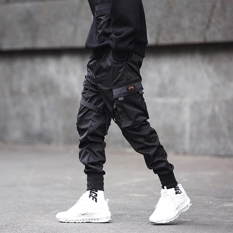 Streetwear cargo pants worn by male model against concrete wall background showcasing side utility pockets and smooth durable fabric texture