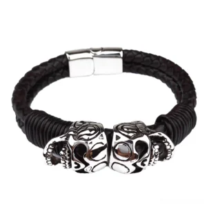 Double skull stainless steel charms on braided black leather bracelet, studio product photography