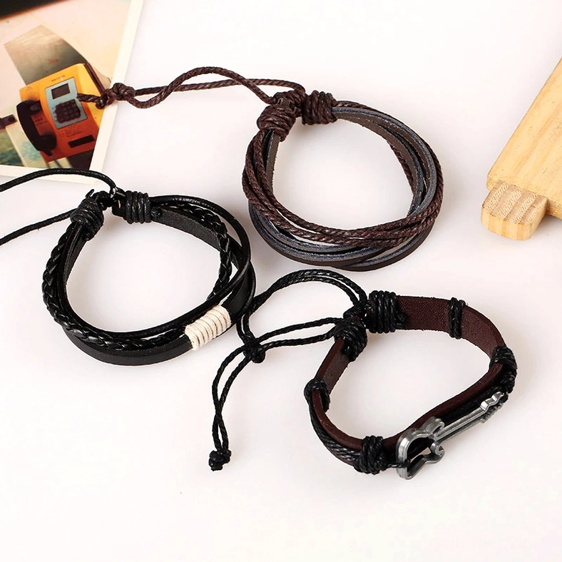 Vintage braided rope leather bracelet set with metal guitar charm and adjustable knot closure, flat lay display showing black and brown leather layers, textile weave detail, and charm pendant on tabletop with decorative background