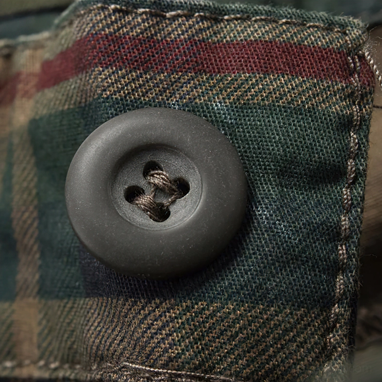 Macro detail of dark plastic button fastening on tartan plaid cargo shorts fabric