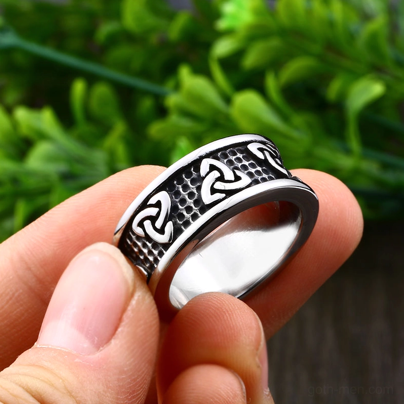 Celtic knot stainless steel ring held in hand with natural green plant backdrop