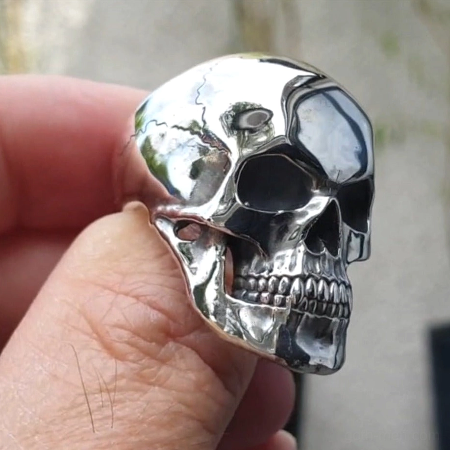 Silver skull ring three-quarter angle on finger showing cracked skull surface design and polished finish