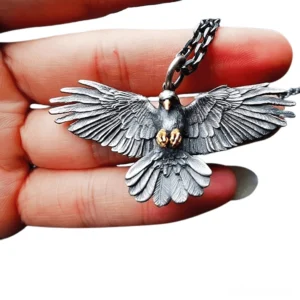 Crow raven pendant held in hand showing oxidized metal finish with front feather details and golden claw accents, side view gothic necklace