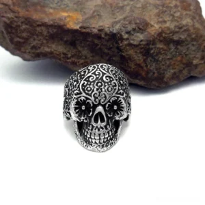 Dark silver gothic skull ring on stone surface, intricate carved floral patterns, punk rock alternative jewelry