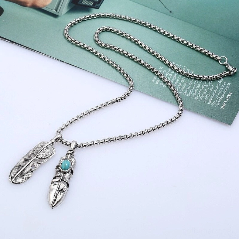 Delicate mini feather pendant with tiny turquoise stone inlay on refined metal chain, desktop product display