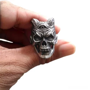 Three-eyed demon skull ring on male hand - gothic stainless steel biker jewelry with horns and fangs