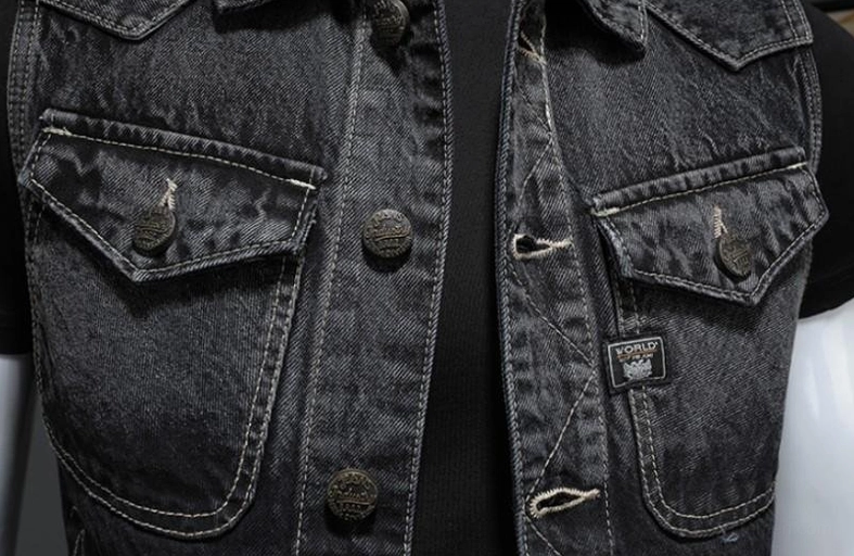 Extreme close-up of denim vest placket showing contrast topstitching, branded button hardware, and pocket tag detail