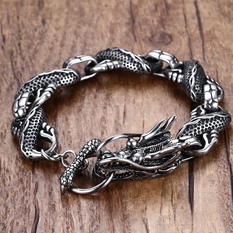 dragon engraved stainless steel bracelet overhead flat lay wooden background detailed dragon link motif