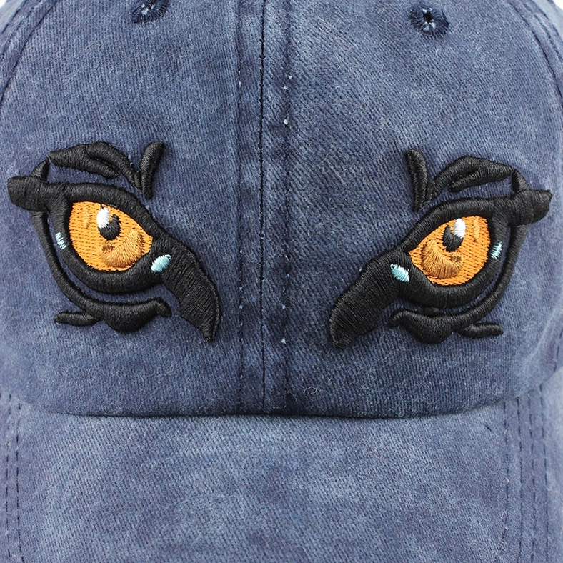 Close-up of double eagle eye embroidery on navy blue gothic cap, detailed 3D stitching