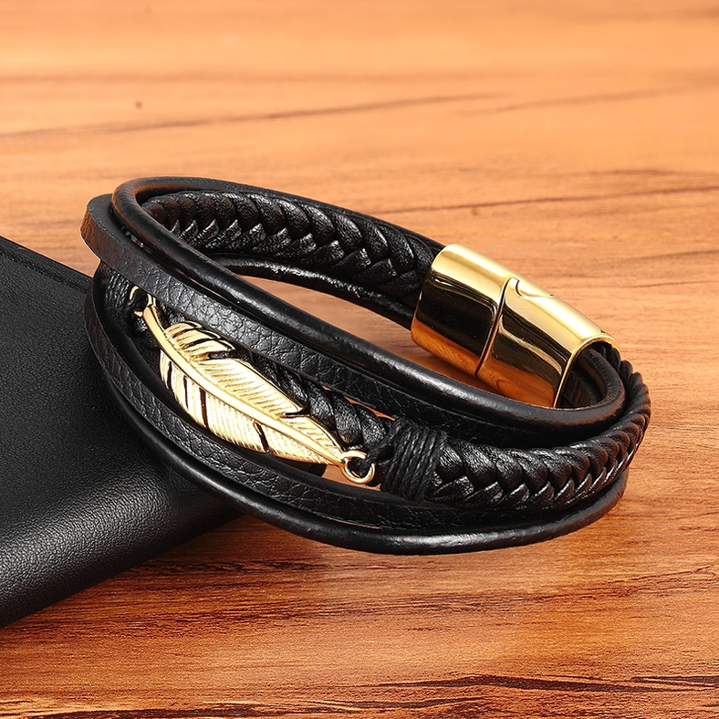 Gold-tone gothic feather leather bracelet on leather accessory background, oblique flat lay angle