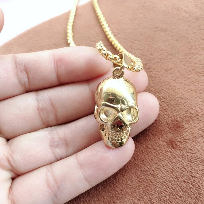 Gold skull pendant necklace side close-up on hand, demonstrating wear and lustre of stainless steel