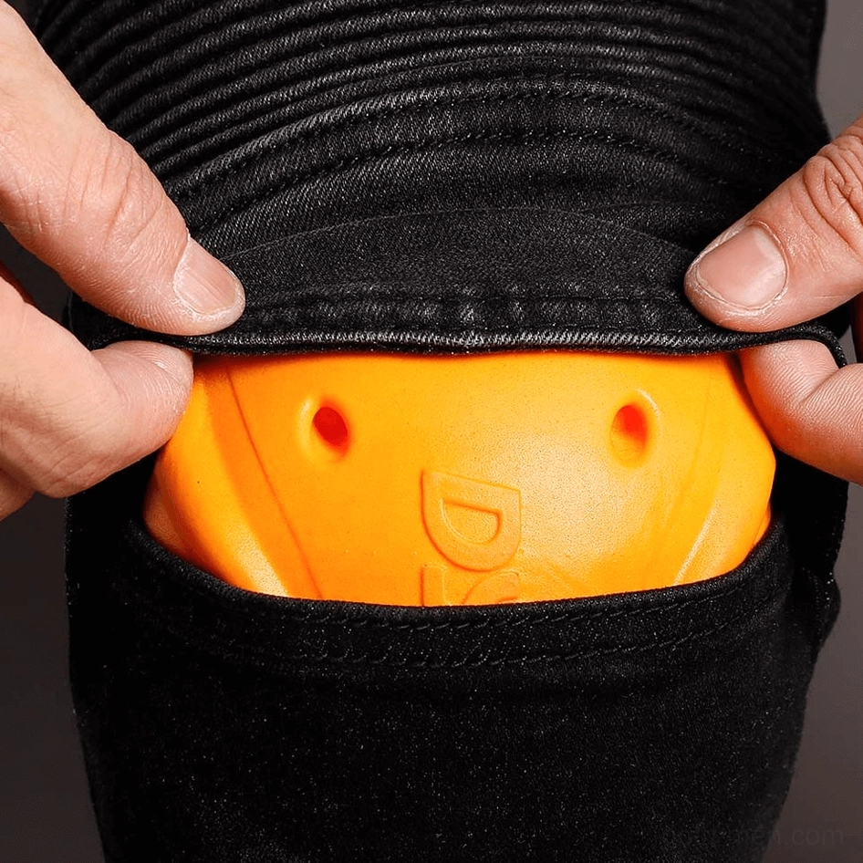 Close-up detail of black gothic biker jeans knee pocket with orange impact-resistant armor pad and ribbed trim