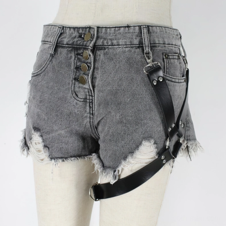 Alternative fashion leg harness with silver metal rivets worn over denim shorts, left front angle