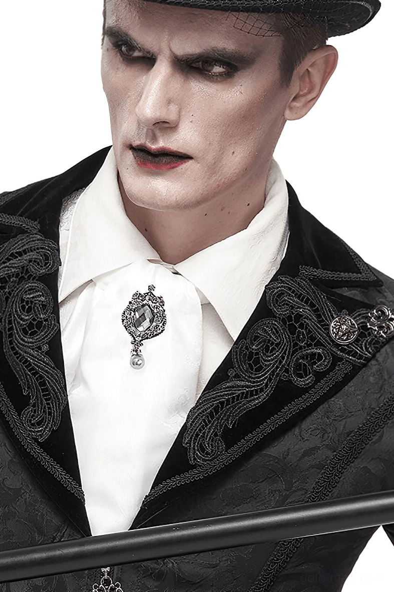 Male goth performer wearing white ascot tie with crystal brooch and black embroidered formal suit