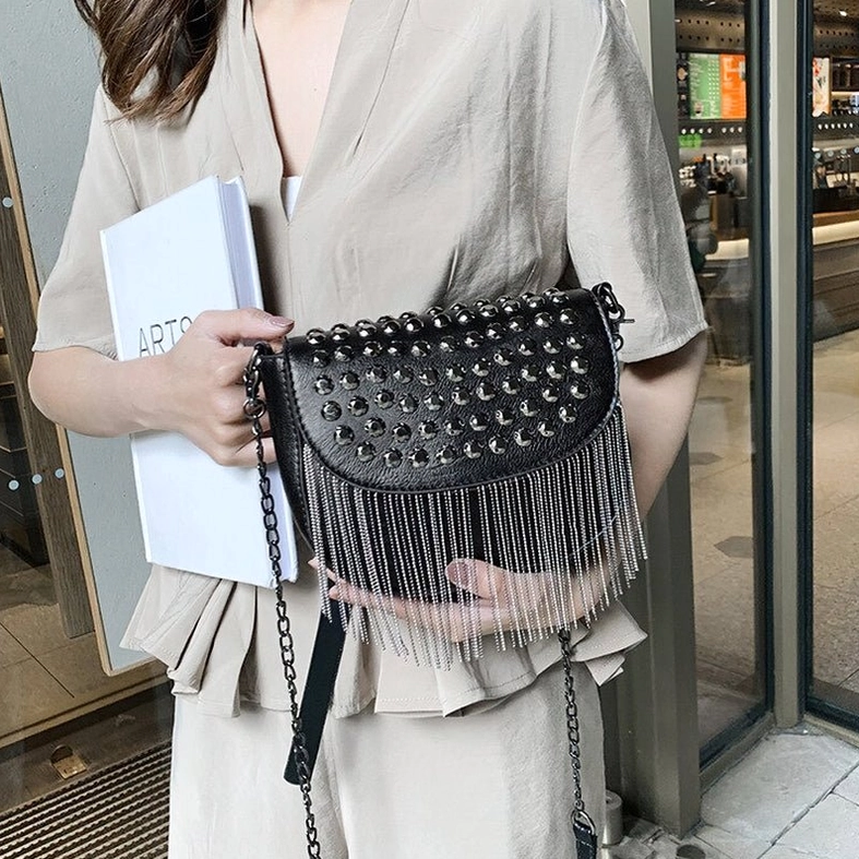 Close-up detail of gothic shoulder bag showing chain strap, fringe trim, and metal rivet studs outdoors