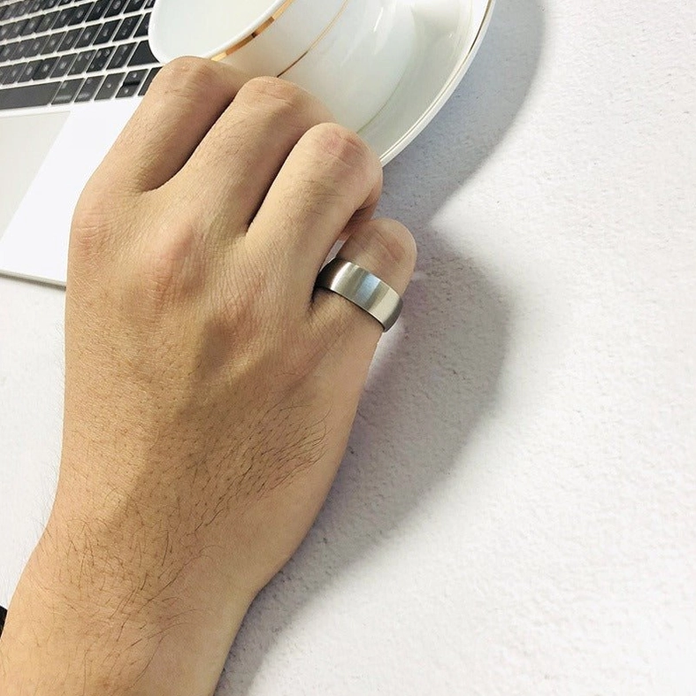 Worn gothic stainless steel matte band ring on male model's index finger in professional office setting, demonstrating minimalist alternative style and everyday wearability