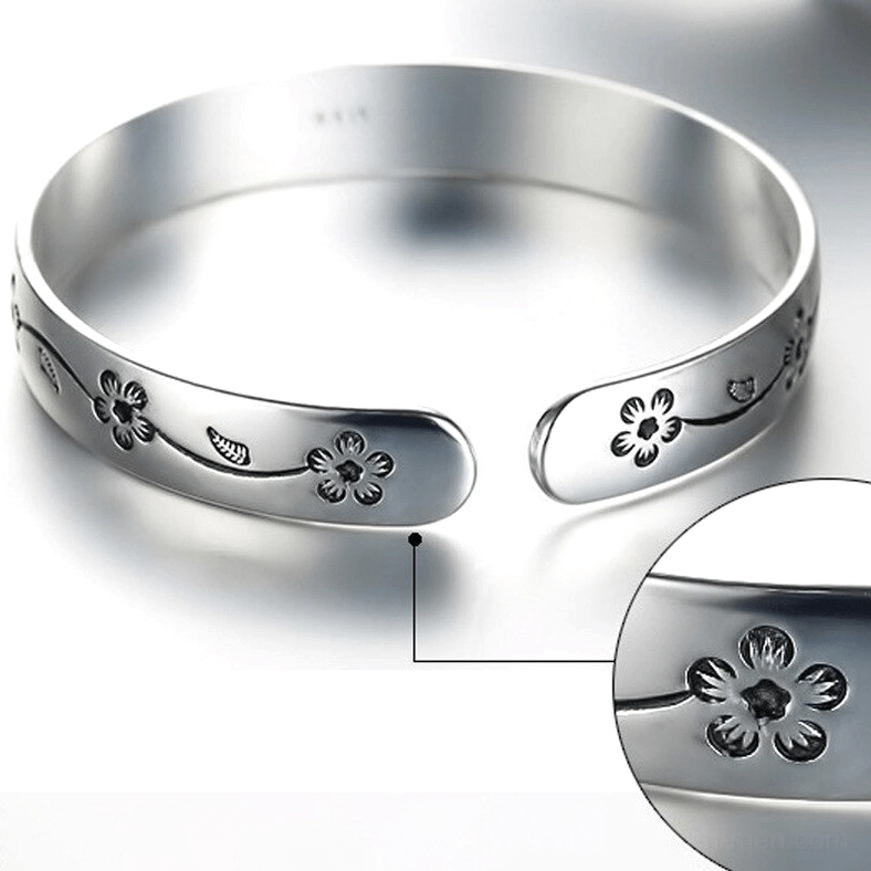 Top-down close-up of gothic open cuff bangle showing inner marking, polished silver surface with engraved flower vine design