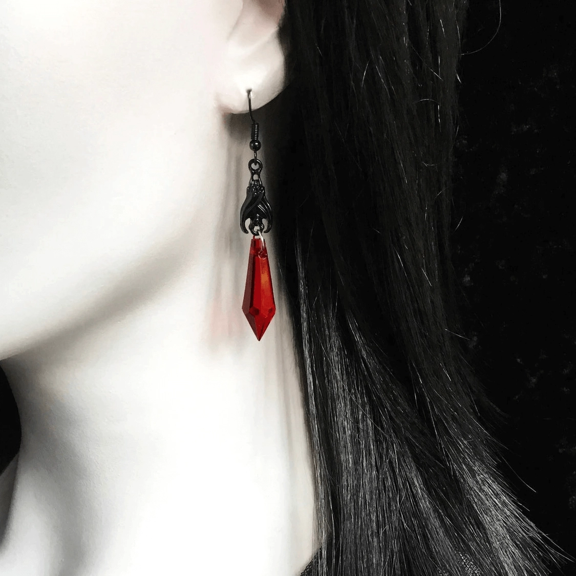 Gothic bat teardrop earring on model - close-up side view showing carved black metal hardware and red pendant