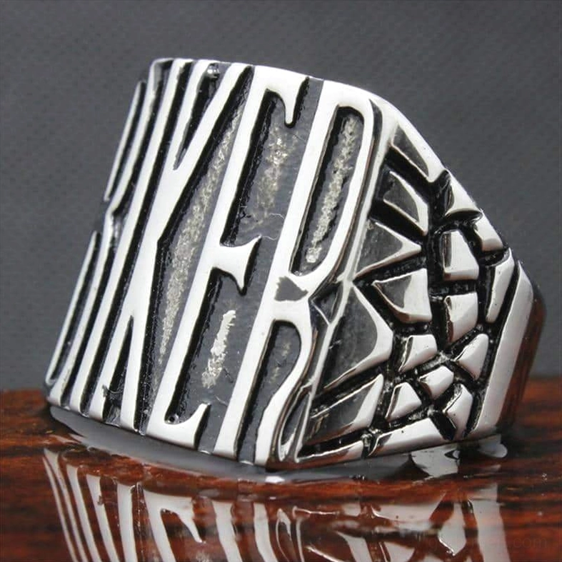 Gothic biker ring tilted angle showing embossed text and textured cracked side design on reflective wooden backdrop
